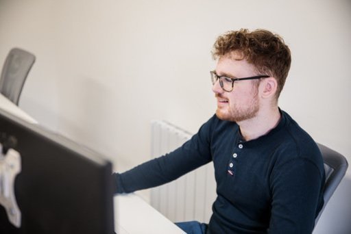 A man sat at a desk, looking at a computer screen