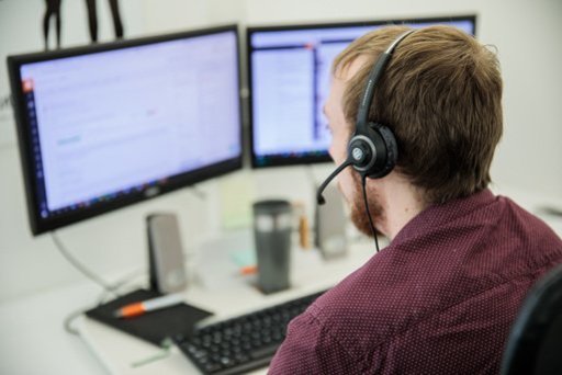 A support worker sat at his computer, wearing a headset